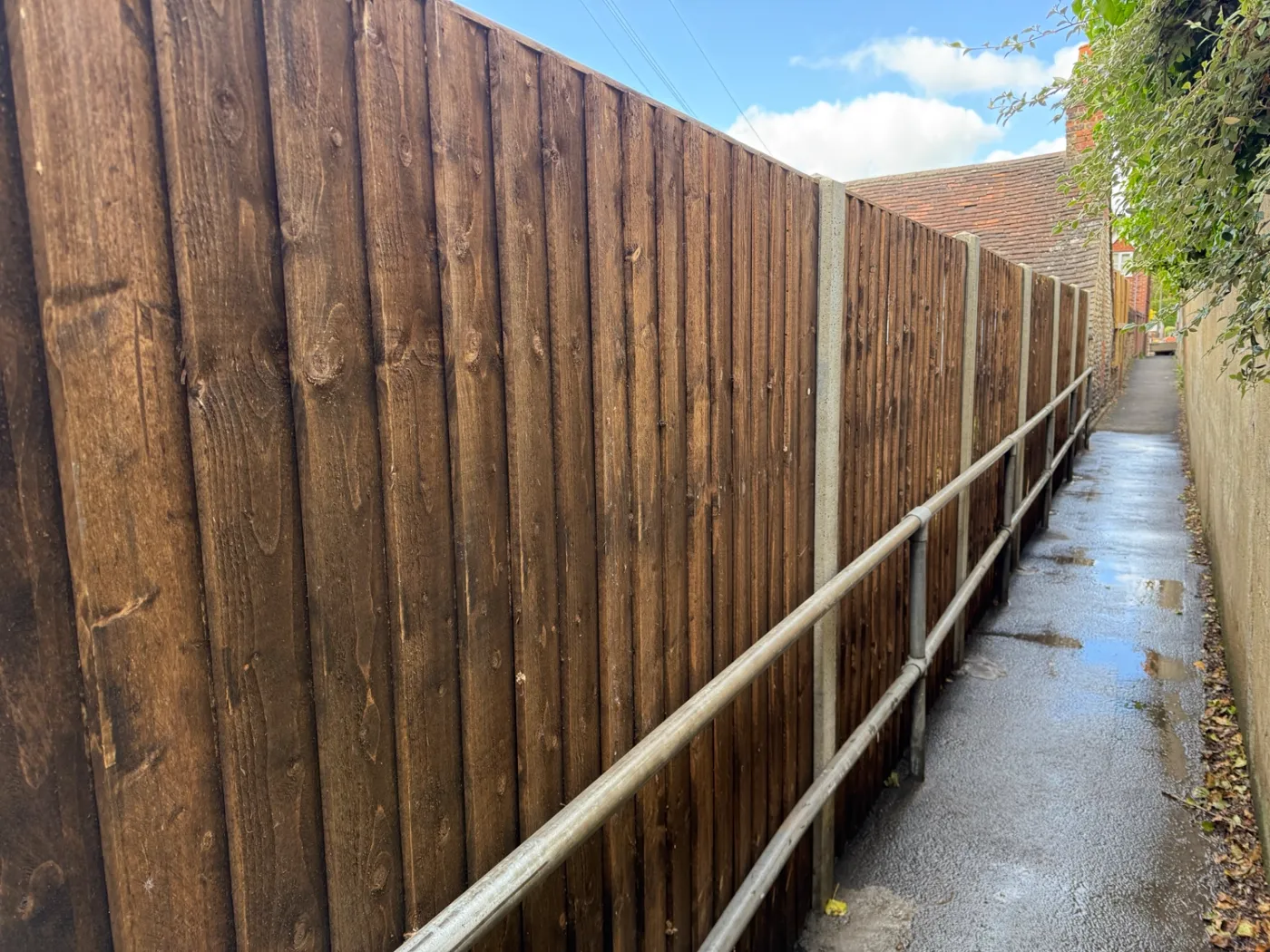Tall dark stained closeboard fence running along an access alleyway