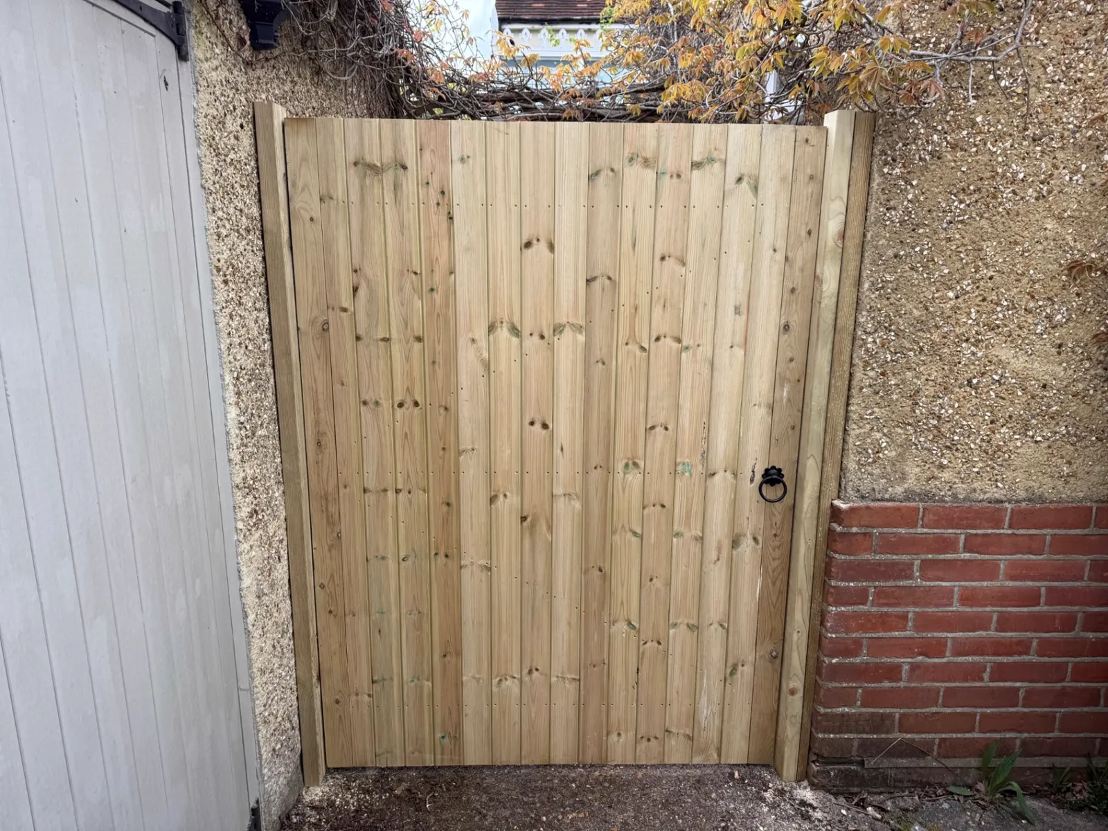 Tongue and groove timber garden gate fitted between a wall and brick pier