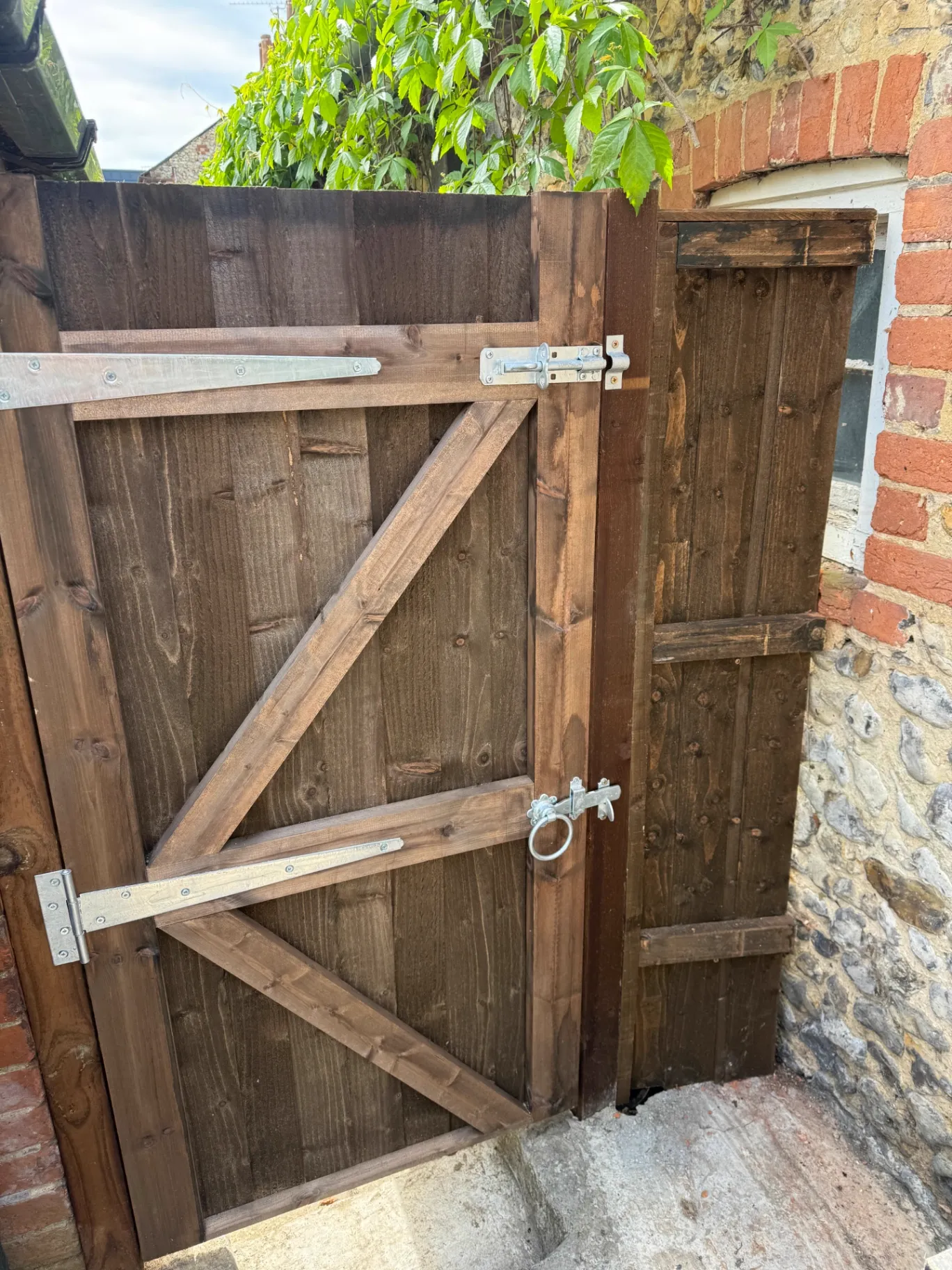 Dark stained braced timber gate with heavy hinges and bolt